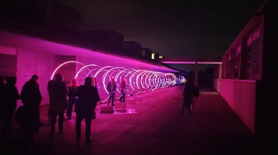 Instalación lumínica con aros LED en Encén Montilivi 2025, con visitantes interactuando en el exterior del campus